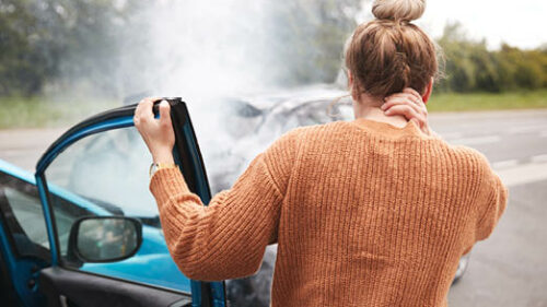 A woman standing in pain with her car that had been in an accident.