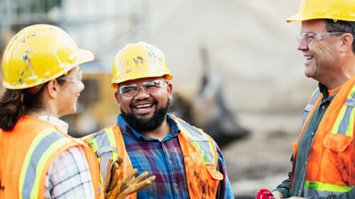 Three construction workers in safety gear talking on a job site.