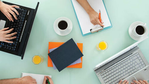 Four people around a table writing in notebooks and typing on computers.