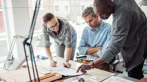 three employees pointing at paperwork on a desk.