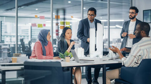 A multicultural group of design professionals discussing a model building in a conference room