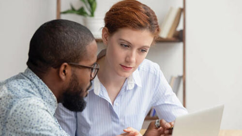 Two employees talking while looking at a laptop.