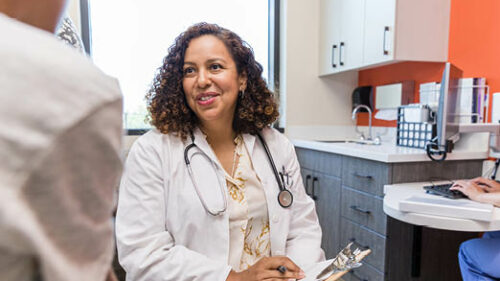 A female doctor talking to a patient in a welcoming exam room.