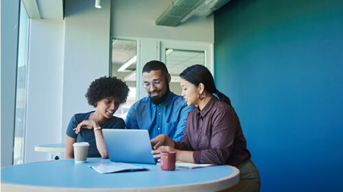 Three happy employees sitting around a laptop.