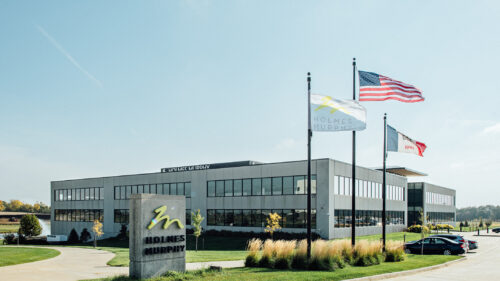 Holmes Murphy office in Waukee with a bright blue sky, green grass and the Holmes Murphy, USA, and Iowa flags blowing in the wind.