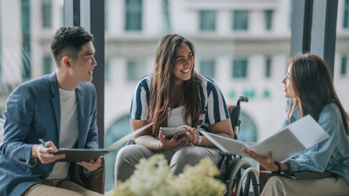 Three employees chatting, one uses a wheelchair.