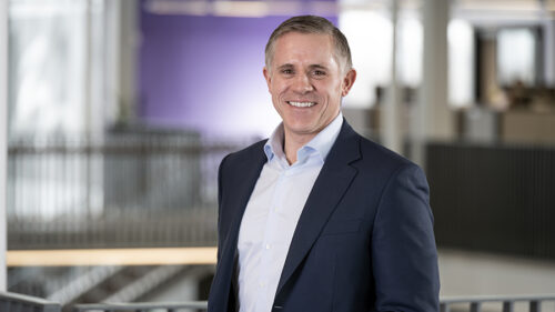 Jay Reavis in a suit jacket and open collar smiling for a professional photo in an office