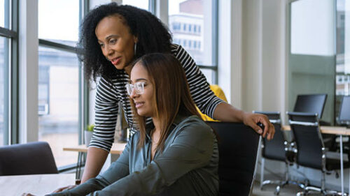 Two female employees looking at a computer together in collaboration