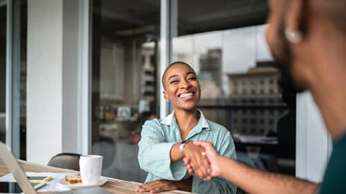 Two people shaking hands over a conference table.