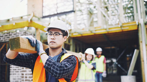 A construction worker holding some beams of wood while working.