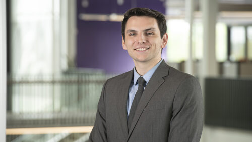 A young man in a grey suit smiling for a professional photo.